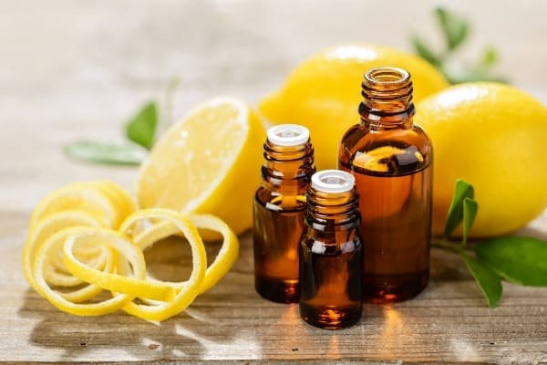 Three bottles of lemon essential oil surrounded by lemons and lemon peels.