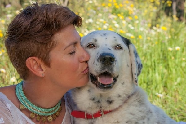 A woman giving a black-and-white dog a kiss on the cheek in front of a flowering field.