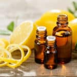 Three bottles of lemon essential oil surrounded by lemons and lemon peels.