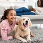 A young girl and her Golden Retriever lying together on a gray area rug.